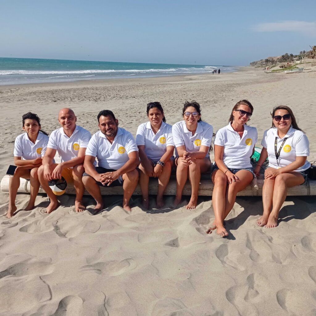 A team of employees of Future of Fish, sitting on a beach in Peru, with the ocean in the background.